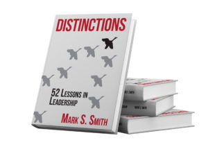 3 stacked books with one book leaning against the stack. Cover of book is gray with V of geese in darker gray, title text is Red (Distinctions by Mark S Smith).